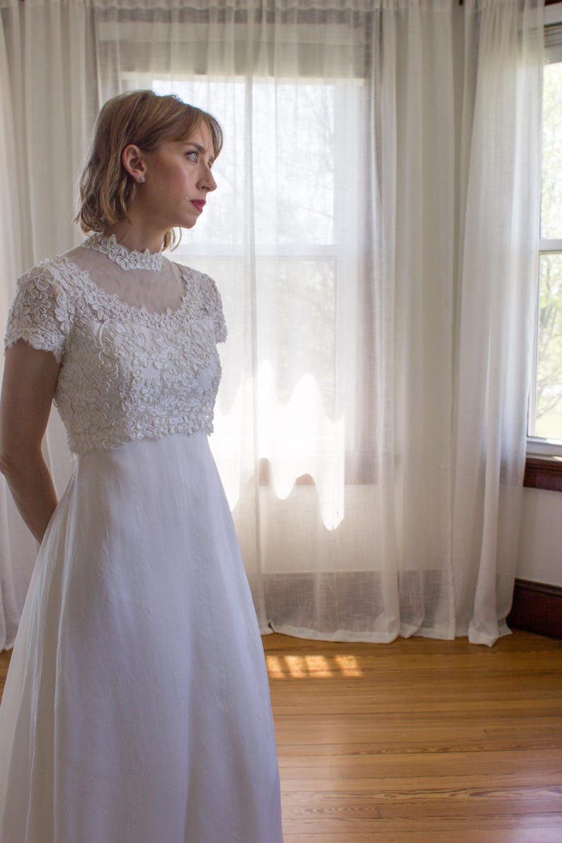 May include: A white lace wedding dress with a high neckline and short sleeves. The dress has a full skirt and is made of a soft, flowing fabric.