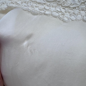 May include: White satin fabric with a white lace trim. The fabric has a small tear in it.