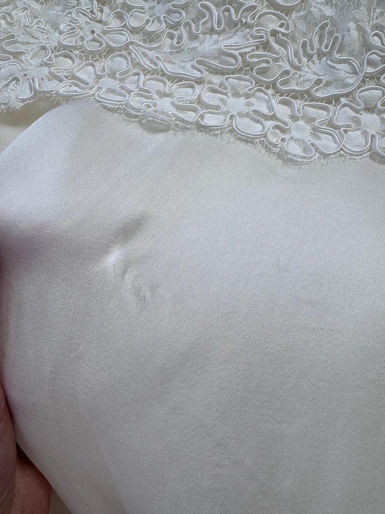 May include: White satin fabric with a white lace trim. The fabric has a small tear in it.