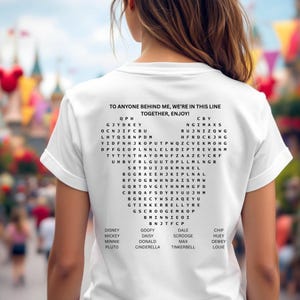 Pode incluir: Camiseta branca com um jogo de palavras em forma de cora&ccedil;&atilde;o e o texto "TO ANYONE BEHIND ME, WE'RE IN THIS LINE TOGETHER, ENJOY!". O jogo inclui nomes de personagens da Disney.