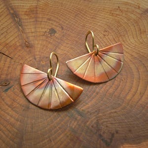 Puede incluir: Un par de pendientes de oro y cobre con un diseño en forma de abanico. Los pendientes están hechos de metal y tienen una superficie texturizada.