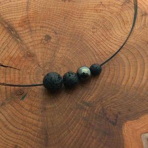 Può includere: Una collana nera con quattro perle rotonde. Tre delle perle sono in pietra lavica nera e una è in ematite grigio scuro.
