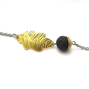 Può includere: Un braccialetto a catena d'argento con un ciondolo a forma di foglia d'oro e una perla di roccia lavica nera.