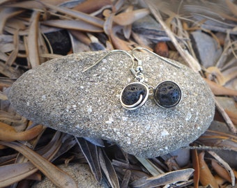 May include: A pair of silver earrings with black lava rock beads. The earrings are hanging from a rock.