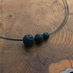 Op de afbeelding: Een zwarte lavasteenketting met drie ronde kralen op een dun zwart koord.