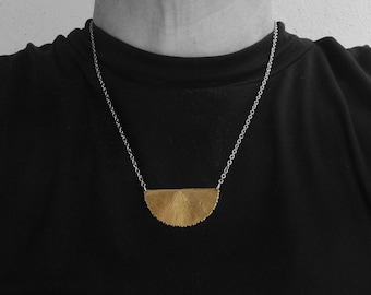 May include: A silver chain necklace with a gold, half-circle pendant. The pendant has a textured, fan-like design.