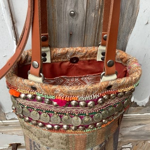 Puede incluir: Un bolso tote de cuero marr&oacute;n con un dise&ntilde;o bordado de colores y detalles plateados. El bolso tiene un asa superior y dos correas largas.