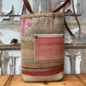 Puede incluir: Un bolso tote grande tejido con un patr&oacute;n de rayas rosa, marr&oacute;n y beige. El bolso tiene una correa de cuero y un peque&ntilde;o bolsillo en la parte delantera.