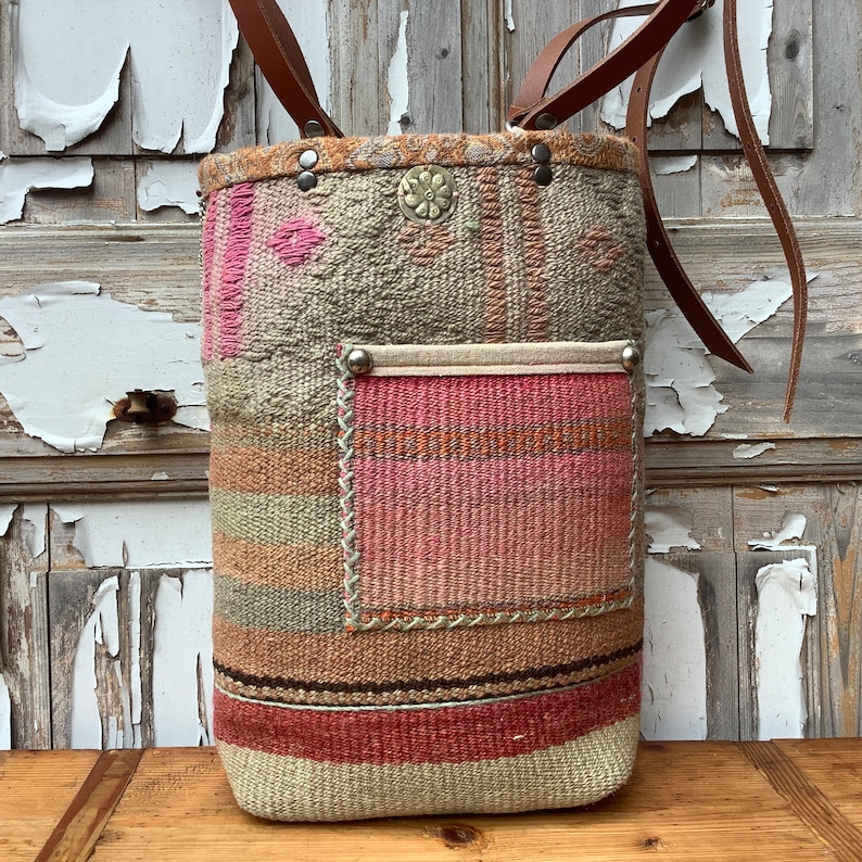 Puede incluir: Un bolso tote grande tejido con un patr&oacute;n de rayas rosa, marr&oacute;n y beige. El bolso tiene una correa de cuero y un peque&ntilde;o bolsillo en la parte delantera.