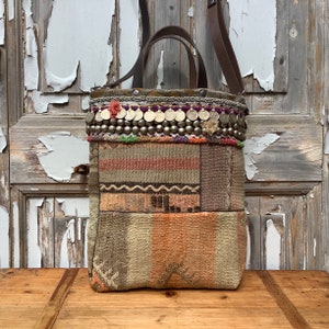 Op de afbeelding: Een patchwork tote bag met een bruine leren band en een zilveren en paarse kralenbies. De tas is gemaakt van verschillende stoffen, waaronder een gestreepte stof, een bloemenstof en een effen stof.