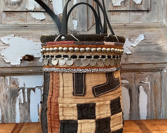 Puede incluir: Bolso tote artesanal con diseño patchwork. El bolso presenta una mezcla de texturas y colores, incluyendo telas negras, marrones y beige. Está adornado con adornos plateados en forma de monedas y tiene asas de cuero negro.