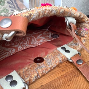 Puede incluir: Un bolso tote de tela marr&oacute;n y beige con una correa de cuero y detalles met&aacute;licos. El bolso tiene un forro estampado y un cierre de presi&oacute;n.