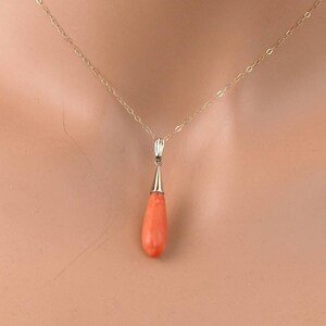 Pu&ograve; includere: Una collana a catena in oro con un ciondolo in corallo liscio a forma di goccia. Il ciondolo &egrave; fissato da un cappuccio in oro lucido sulla parte superiore, che si collega a una delicata catena a maglie d'oro attorno al collo.