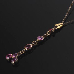 May include: A gold chain necklace featuring a vertical drop pendant set with five oval-cut purple gemstones. The pendant consists of a single line of four stones leading to a cluster of three stones at the base, all held in gold settings.