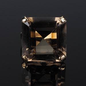 May include: A square-shaped, clear, smoky quartz ring with gold accents.