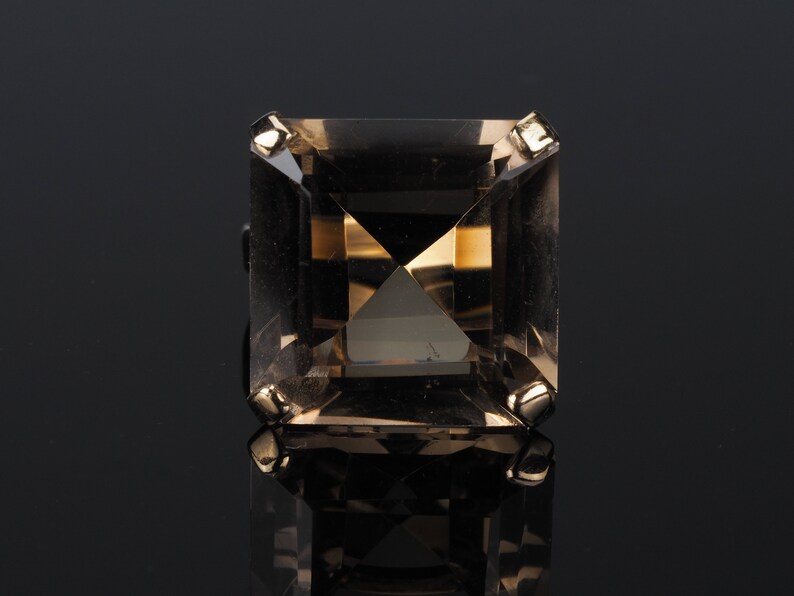 May include: A square-shaped, clear, smoky quartz ring with gold accents.