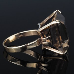 May include: A gold ring with a large, clear, faceted gemstone. The ring is set in a simple, elegant style.