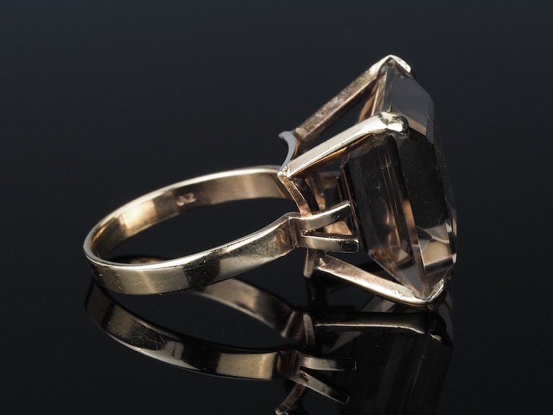 May include: A gold ring with a large, clear, faceted gemstone. The ring is set in a simple, elegant style.