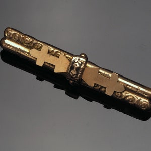 Gold filled bar brooch with scroll decoration and has a black enamel applied decoration with symbols applied.