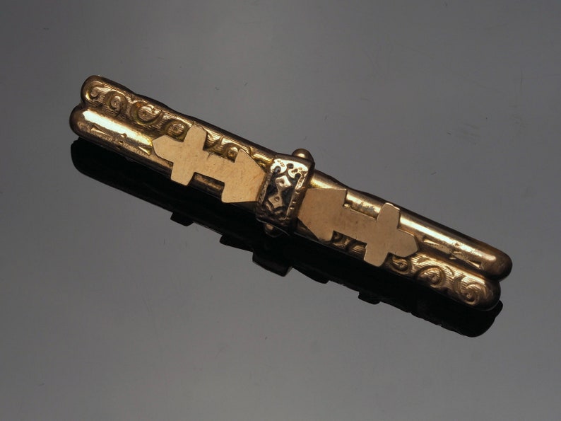 Gold filled bar brooch with scroll decoration and has a black enamel applied decoration with symbols applied.