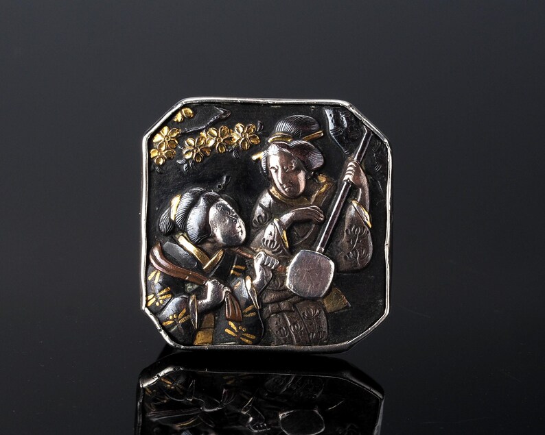 An antique brooch pin which depicts two Japanese Geisha girls in the Shakudo technique. This panel was made in the Meiji period by the Samurai makers of Samurai armour.