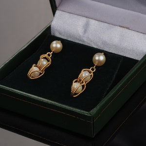 These attractive 9k gold earrings have a pearl with a dangling two caged pearls pendant. The caged pearls are enclosed or wrapped in gold rope. The pearls are cultured. The earrings have gold butterfly backs. The gold rope has a matte sheen to it.