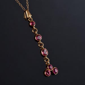May include: A gold pendant necklace featuring a vertical chain of six bezel-set, round and cushion-cut deep pink gemstones. The pendant hangs from a delicate gold chain, with the bottom section branching into a cluster of three stones.