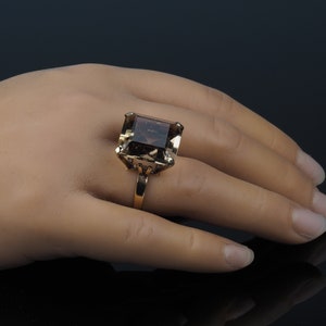 May include: A gold ring with a large, square-shaped, smoky quartz gemstone.