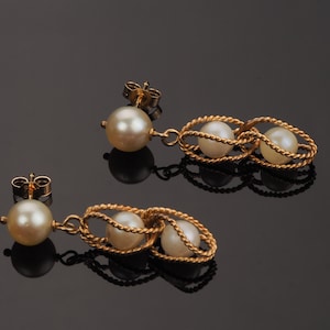 May include: A pair of gold earrings with a pearl drop and two pearls in a twisted gold cage design.
