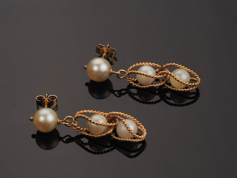 May include: A pair of gold earrings with a pearl drop and two pearls in a twisted gold cage design.