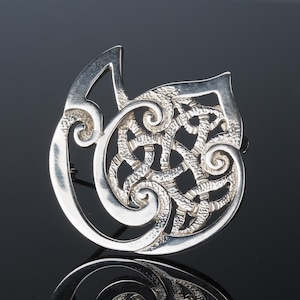 May include: A silver brooch with a Celtic knot design. The knot is intricate and detailed, and the brooch is a beautiful example of Celtic craftsmanship.