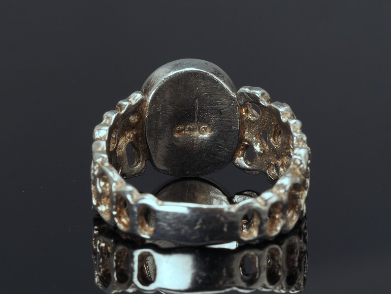 May include: Silver ring with a round, textured band and a smooth, round stone. The ring is marked with the number "925" on the inside of the band.
