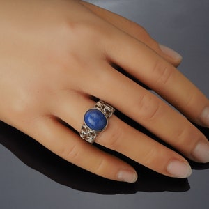 May include: A silver ring with a blue oval gemstone set in a chain-link band.