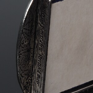 May include: A silver picture frame with a decorative border featuring a floral design and the inscription "In the shadow of the moon".