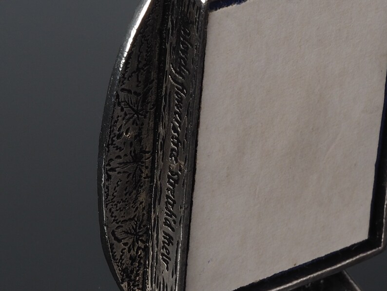 May include: A silver picture frame with a decorative border featuring a floral design and the inscription "In the shadow of the moon".