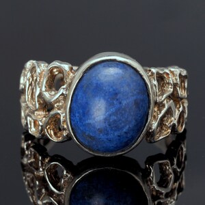 May include: A silver ring with a blue gemstone set in a textured band.