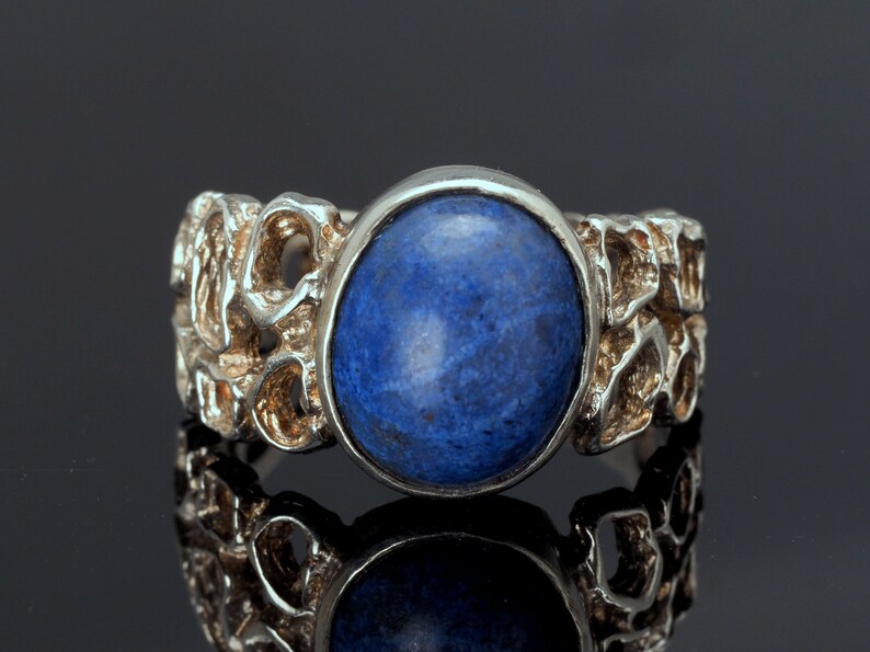 May include: A silver ring with a blue gemstone set in a textured band.