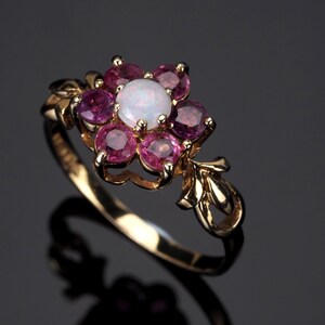 Puede incluir: Un anillo de oro con un dise&ntilde;o floral. El centro de la flor es un &oacute;palo blanco, rodeado de seis piedras preciosas rosas. El anillo tiene una banda delicada de inspiraci&oacute;n floral.