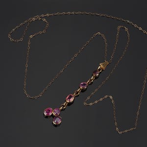 May include: A gold chain necklace featuring a vertical drop pendant set with six oval-shaped pink gemstones. The pendant consists of a single line of four stones leading to a base with two additional stones arranged in a cluster at the bottom.