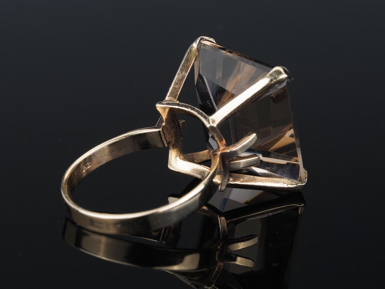 May include: A gold ring with a large, clear, faceted gemstone. The gemstone is set in a prong setting and has a square shape.