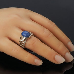 May include: A silver ring with a blue oval gemstone set in a delicate, openwork band.