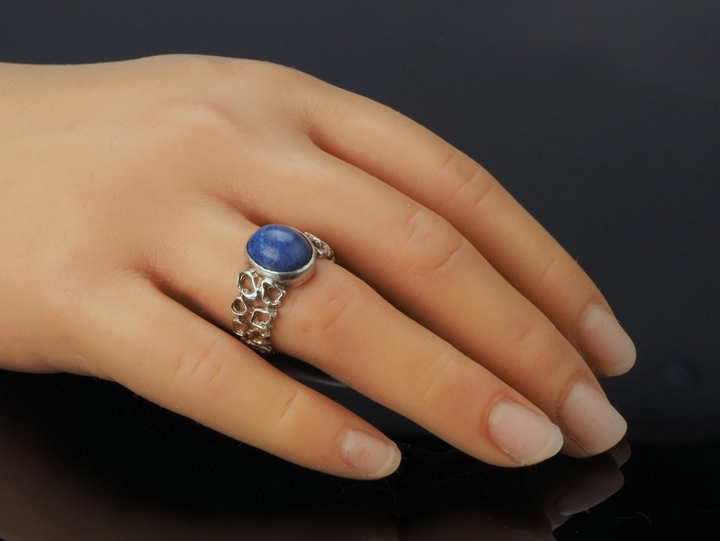 May include: A silver ring with a blue oval gemstone set in a delicate, openwork band.