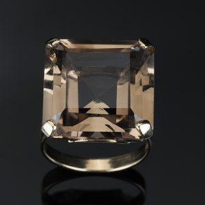 May include: A gold ring with a large, square-shaped, light brown gemstone.