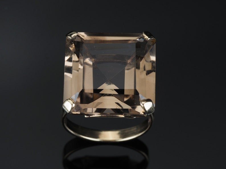 May include: A gold ring with a large, square-shaped, light brown gemstone.