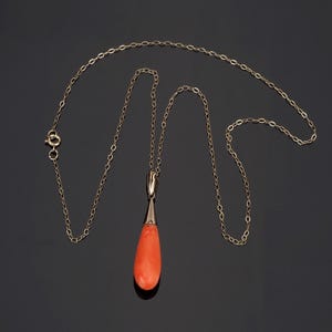 Pu&ograve; includere: Una collana a catena in oro con un ciondolo a forma di goccia realizzato in corallo arancione liscio e vibrante. Il ciondolo &egrave; fissato alla catena tramite una contromaglia in oro lucido e la collana include una piccola chiusura a molla.