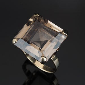 May include: A gold ring with a large, square-shaped, smoky quartz gemstone.