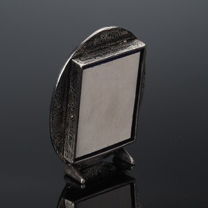 May include: A silver-toned oval picture frame with a textured surface and a small stand. The frame has a blue and white border and the text "The Pleasant Street Shop" is engraved on the side.