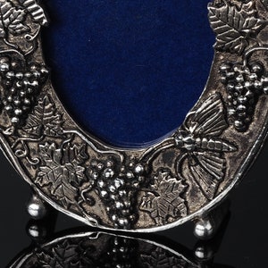 May include: Silver-toned picture frame with a blue velvet backing. The frame is decorated with a grapevine design and a butterfly.