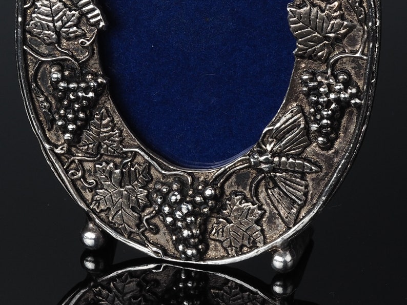 May include: Silver-toned picture frame with a blue velvet backing. The frame is decorated with a grapevine design and a butterfly.