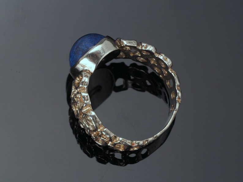 May include: A silver ring with a blue gemstone set in a textured band.